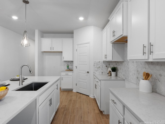 kitchen with sink, hanging light fixtures, light hardwood / wood-style floors, light stone counters, and white cabinetry