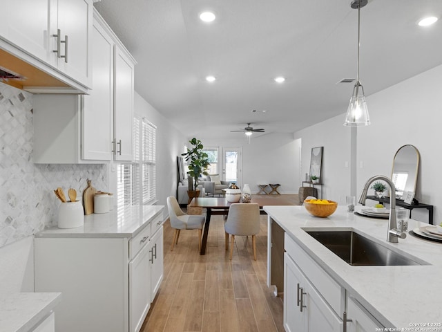 kitchen with pendant lighting, white cabinets, sink, ceiling fan, and light stone countertops