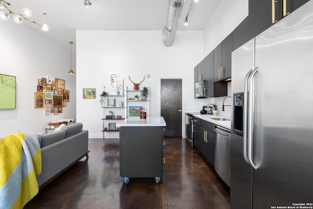 kitchen featuring a center island, sink, a towering ceiling, decorative light fixtures, and stainless steel appliances