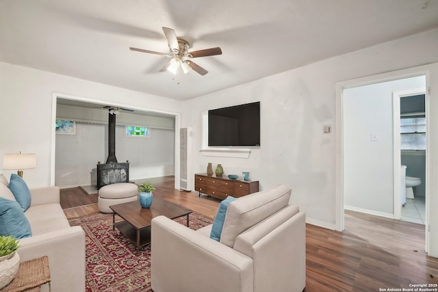 living room featuring dark hardwood / wood-style flooring, a wood stove, and ceiling fan