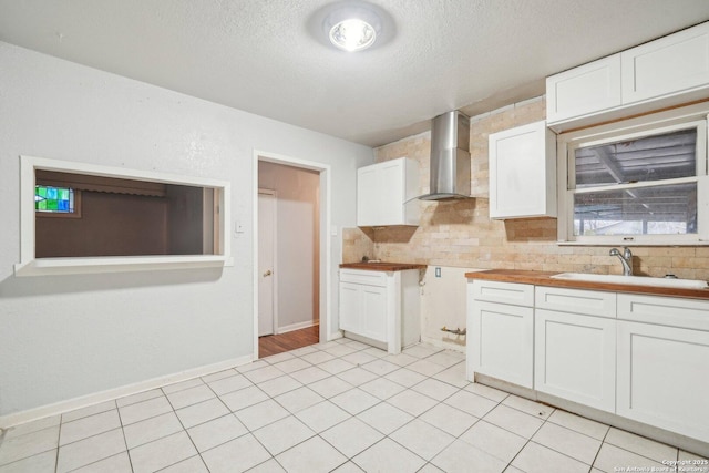 kitchen featuring butcher block countertops, white cabinetry, sink, and wall chimney exhaust hood