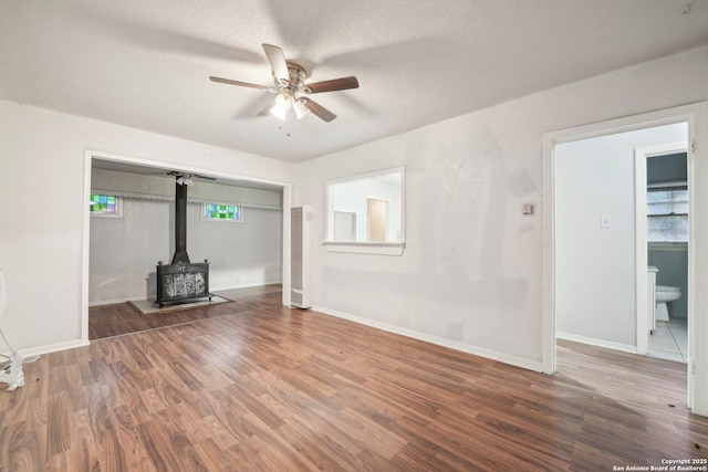 unfurnished living room with a textured ceiling, dark hardwood / wood-style flooring, a wood stove, and ceiling fan