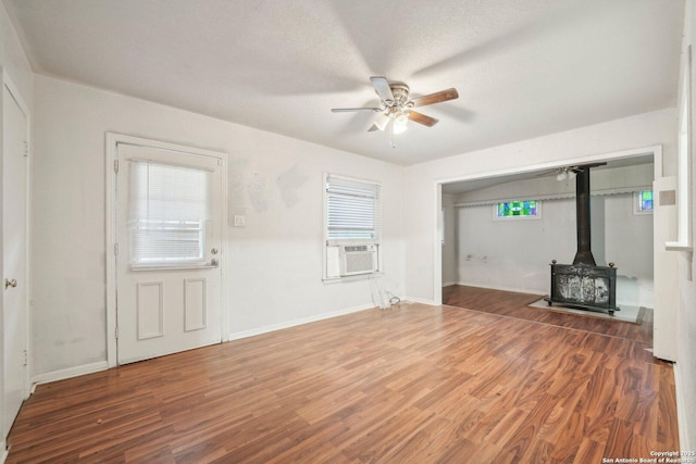 unfurnished living room featuring plenty of natural light, cooling unit, a wood stove, and dark wood-type flooring