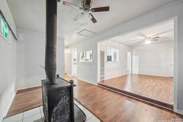 living room featuring light tile patterned floors, a wood stove, ceiling fan, and a healthy amount of sunlight