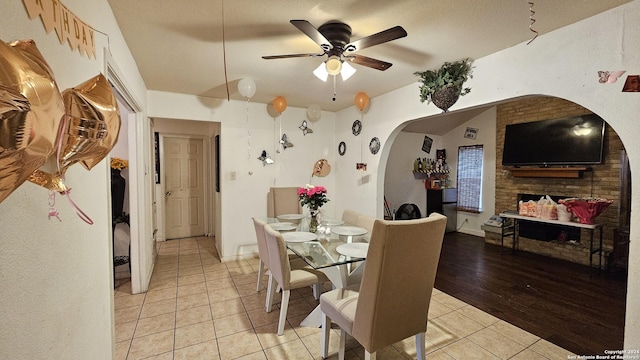 dining room with ceiling fan, a large fireplace, and light tile patterned floors