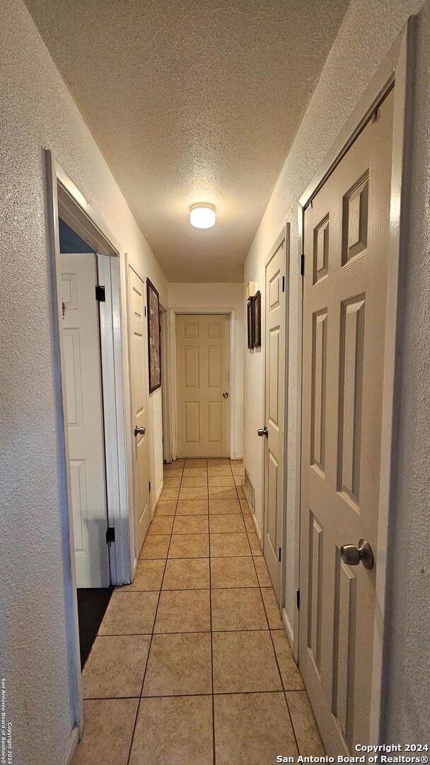 hallway with a textured ceiling and light tile patterned flooring