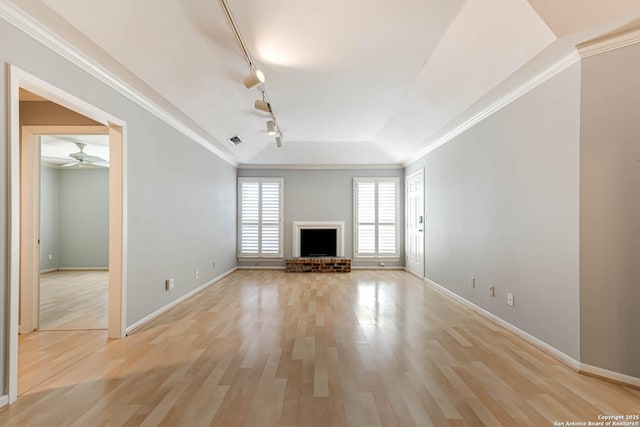 unfurnished living room with ceiling fan, a brick fireplace, ornamental molding, track lighting, and light wood-type flooring