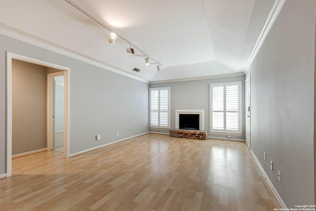 unfurnished living room featuring rail lighting, light hardwood / wood-style floors, a tray ceiling, a fireplace, and ornamental molding