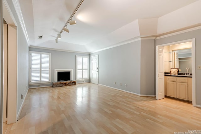 unfurnished living room with light wood-type flooring, rail lighting, a brick fireplace, vaulted ceiling, and crown molding