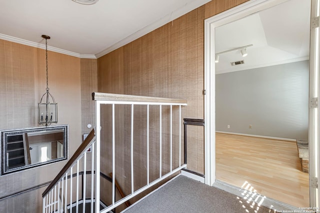 hallway with wood-type flooring, track lighting, an inviting chandelier, and crown molding