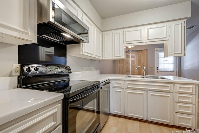 kitchen with black electric range oven, white cabinets, sink, light wood-type flooring, and kitchen peninsula