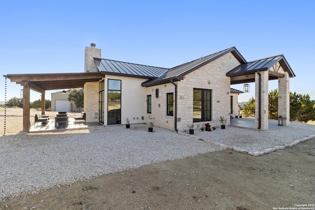 back of property with metal roof, a standing seam roof, and a patio area