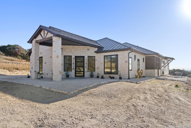 rear view of house with a standing seam roof, stone siding, and metal roof