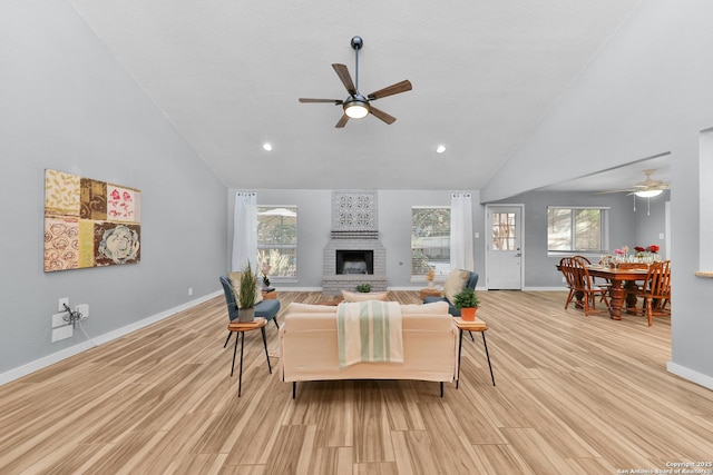 living room with a brick fireplace, ceiling fan, high vaulted ceiling, and light wood-type flooring