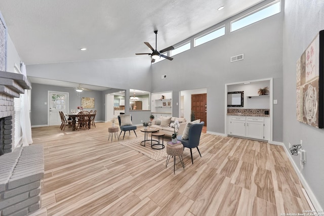 living room featuring ceiling fan, a towering ceiling, a fireplace, and light hardwood / wood-style flooring