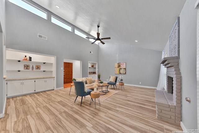 sitting room with light wood-type flooring, a brick fireplace, a textured ceiling, ceiling fan, and a high ceiling