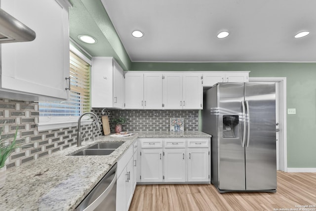 kitchen with appliances with stainless steel finishes, backsplash, light stone counters, sink, and white cabinets