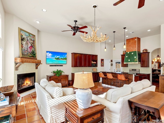 tiled living room with a tile fireplace and ceiling fan with notable chandelier