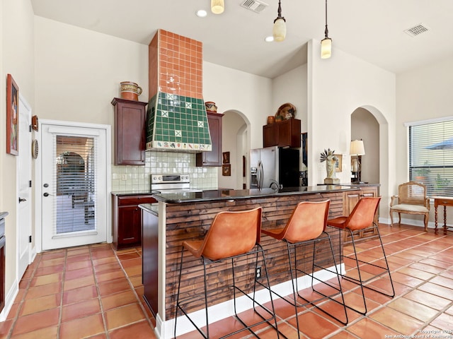 kitchen with decorative backsplash, custom exhaust hood, a breakfast bar, stainless steel appliances, and decorative light fixtures