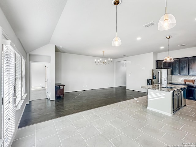 kitchen featuring light stone countertops, sink, stainless steel fridge with ice dispenser, pendant lighting, and a kitchen island with sink