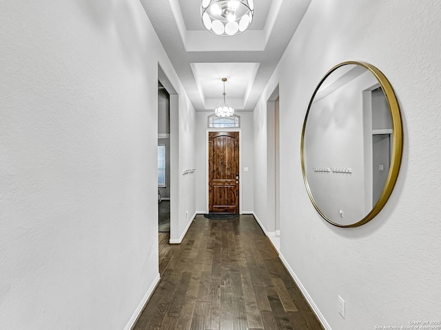 corridor with dark hardwood / wood-style flooring, a raised ceiling, and a notable chandelier