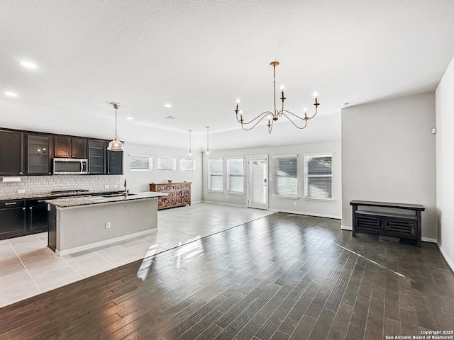 kitchen with an inviting chandelier, tasteful backsplash, light stone counters, pendant lighting, and a kitchen island with sink