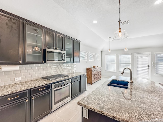 kitchen with pendant lighting, an island with sink, appliances with stainless steel finishes, and vaulted ceiling