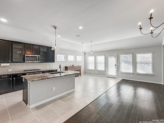 kitchen featuring light stone countertops, appliances with stainless steel finishes, sink, decorative light fixtures, and an island with sink