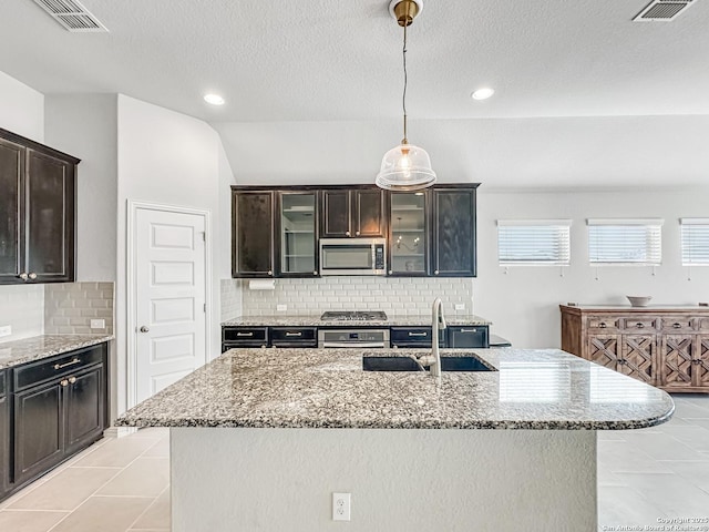 kitchen with sink, vaulted ceiling, decorative backsplash, a center island with sink, and appliances with stainless steel finishes