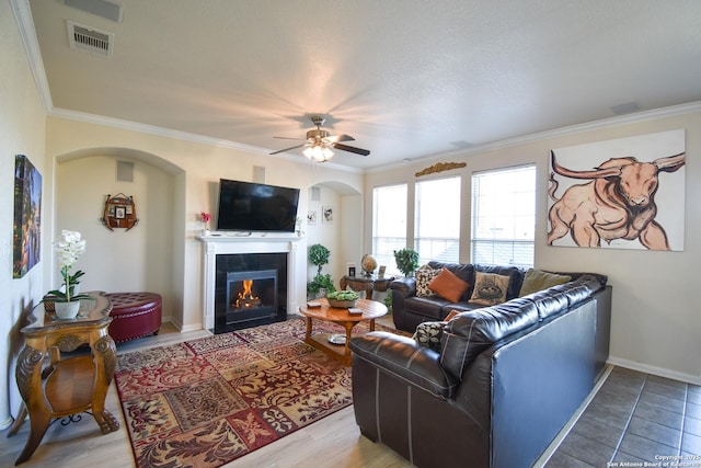 living room featuring a textured ceiling, ceiling fan, crown molding, and a fireplace