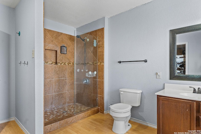 bathroom featuring a tile shower, vanity, wood-type flooring, and toilet