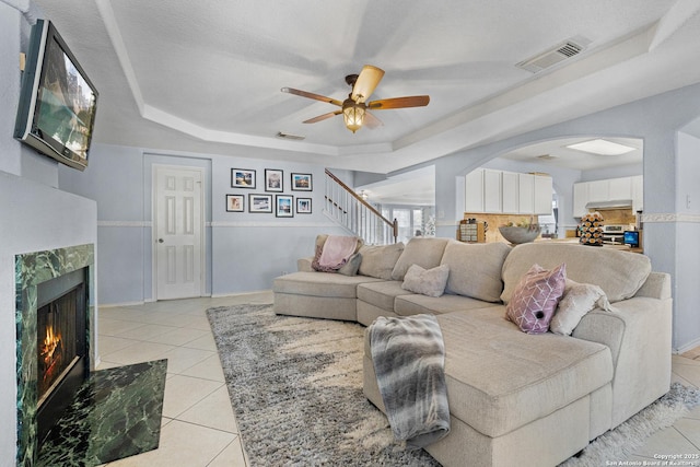 tiled living room featuring ceiling fan, a raised ceiling, and a fireplace