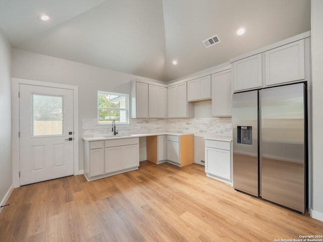 kitchen with stainless steel refrigerator with ice dispenser, light wood-type flooring, vaulted ceiling, sink, and white cabinets