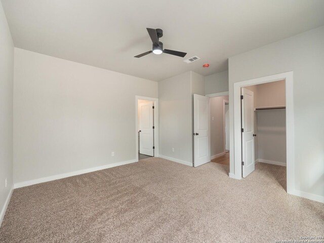 unfurnished bedroom with ceiling fan, a closet, light colored carpet, and a spacious closet