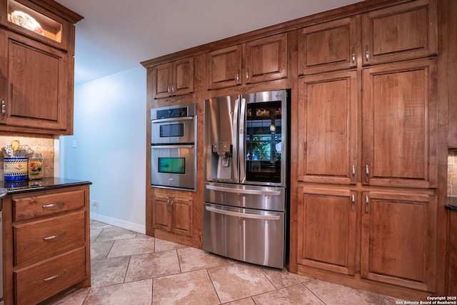 kitchen featuring dark stone countertops, light tile patterned floors, stainless steel appliances, and tasteful backsplash