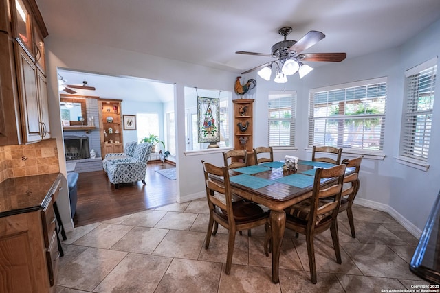 dining area featuring tile patterned flooring, ceiling fan, and a brick fireplace