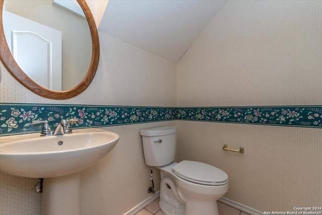 bathroom featuring tile patterned flooring, toilet, sink, and vaulted ceiling