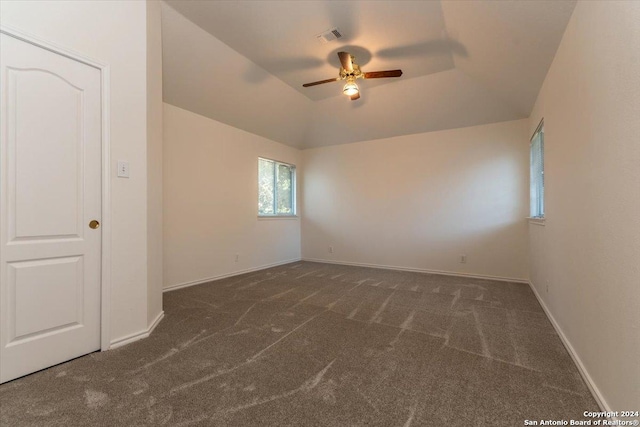 unfurnished bedroom featuring dark colored carpet, a tray ceiling, ceiling fan, and lofted ceiling