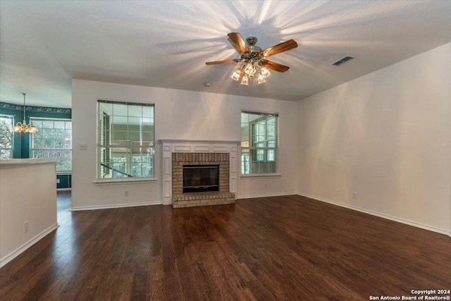 unfurnished living room featuring dark hardwood / wood-style flooring, ceiling fan with notable chandelier, and a brick fireplace