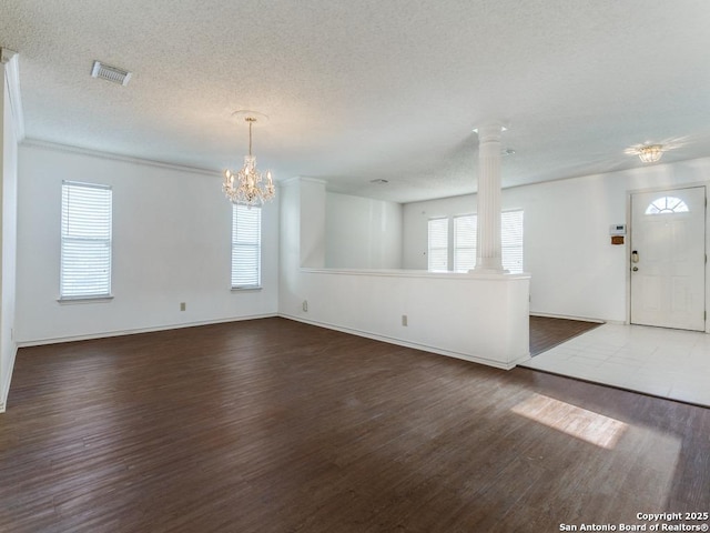 empty room featuring a textured ceiling, dark wood-type flooring, decorative columns, and a chandelier