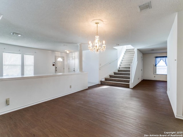 unfurnished living room featuring ornate columns, a textured ceiling, a notable chandelier, and dark hardwood / wood-style flooring