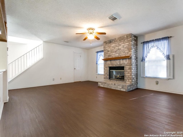 unfurnished living room featuring ceiling fan, dark hardwood / wood-style floors, a brick fireplace, and a textured ceiling