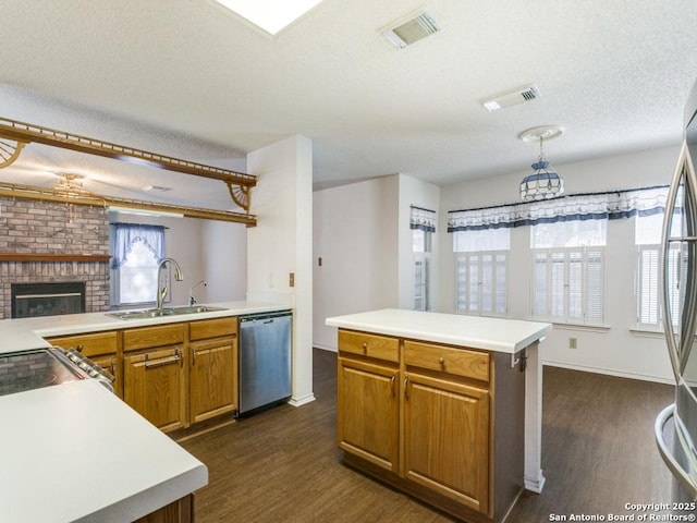 kitchen featuring sink, a center island, a brick fireplace, a textured ceiling, and appliances with stainless steel finishes