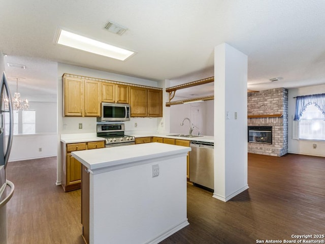 kitchen featuring a kitchen island, sink, a chandelier, stainless steel appliances, and a brick fireplace