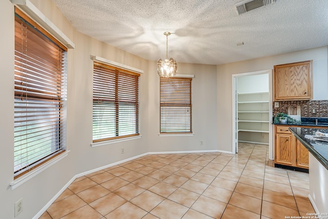 unfurnished dining area featuring light tile patterned floors, a textured ceiling, and a chandelier