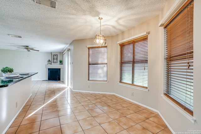 unfurnished dining area with ceiling fan with notable chandelier, light tile patterned floors, and a textured ceiling