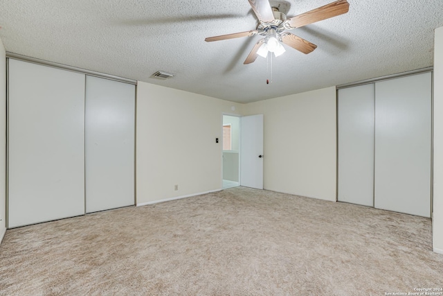 unfurnished bedroom with multiple closets, ceiling fan, light carpet, and a textured ceiling