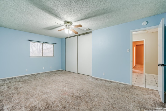 unfurnished bedroom with light carpet, a textured ceiling, a closet, and ceiling fan