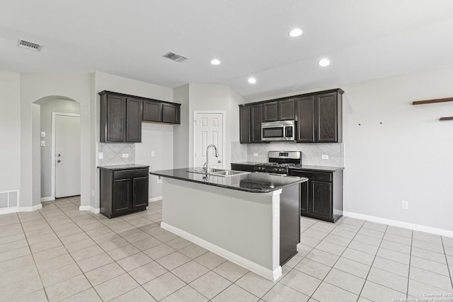 kitchen featuring decorative backsplash, appliances with stainless steel finishes, sink, light tile patterned floors, and an island with sink