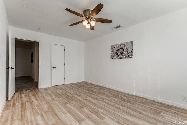 unfurnished bedroom featuring ceiling fan, a closet, a textured ceiling, and light wood-type flooring